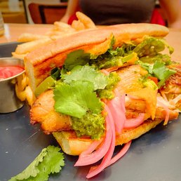 Peruvian Pork Belly Sandwich - A sandwich with grilled chicken, fresh cilantro, pickled onions, and green sauce on toasted bread, served with French fries and ketchup.