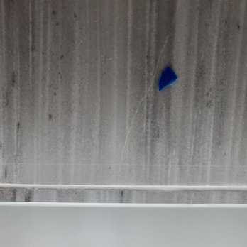 Centex Bath - Crack or scratch in our marble tile - A gray tiled wall shows a visible crack or scratch with a small blue fragment attached or embedded in it. - General Contractors Near Me - Round Rock, Texas