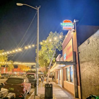 Laguna Burger - Nighttime image of Laguna Burger, a casual eatery, with its illuminated sign reading 'World Famous Laguna Burger.' String lights are hung across the street, creating a warm ambiance. The sidewalk features a trash can, trees, and pedestrians, with parked cars lining the street. The scene captures a relaxed, evening atmosphere in an urban setting. - Burgers Near Me - Albuquerque, New Mexico