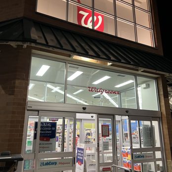 Walgreens - The image shows the exterior of a Walgreens store at night, featuring glass doors and windows. The store's signage is visible, including the Walgreens logo and a sign advertising free COVID-19 vaccines. The interior is brightly lit, revealing shelves and checkout areas inside. The storefront has a brick facade with a metal awning above the entrance. There are security cameras and a small ramp for accessibility at the entrance. - Cosmetics & Beauty Supply Near Me - Severna Park, Maryland
