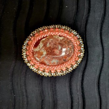 Beaded Iris - Beaded broach - A beaded brooch featuring a central polished stone surrounded by pink and gold beads, placed on black fabric. - Arts & Crafts Near Me - Albuquerque, New Mexico