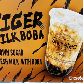 Sharetea - Drink - The image features a promotional sign for Tiger Milk Boba, with bold black text on an orange background. The sign highlights flavors such as brown sugar and fresh milk with boba. A large, clear plastic cup filled with milk tea and tapioca pearls is prominently displayed on the right side of the sign, with branding for Sharetea and details about the establishment. - Bubble Tea Near Me - Phoenix, Arizona