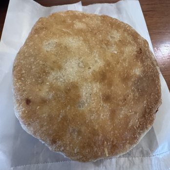 Ming Wei - Ming Wei Fried Chicken Pie - A fried chicken pie with a round, golden-brown, crispy crust is shown resting on a piece of white paper. The crust appears flaky and textured, with some uneven coloring and small bubbles. The pie is placed on a wooden surface, suggesting it is served in a restaurant or takeout setting. The image emphasizes the crust's texture and the pie's size. - Chinese Near Me - Queens, New York