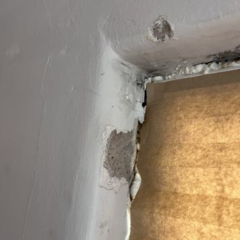 Flawless Results - The image shows a section of a wall with visible damage, including peeling paint, exposed drywall, and areas where the plaster or paint has chipped away. The damage appears to be near a corner or edge, with some areas showing cracks and rough surfaces. The wall's surface is uneven, and there are signs of wear and tear, possibly from moisture or impact. - Windows Installation Near Me - Albuquerque, New Mexico