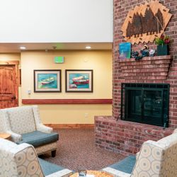 Mill View Memory Care - Cozy common area at Mill View Memory Care in Bend, Oregon, featuring a brick fireplace, comfortable seating, and charming artwork.
