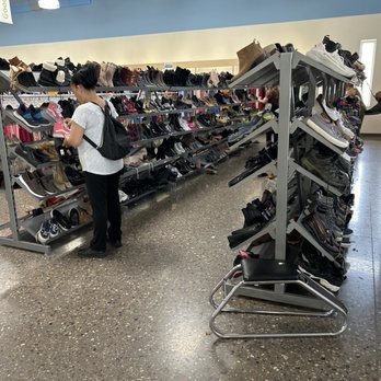 Goodwill - Shoes - Inside a retail store, metal shoe racks display various footwear, with customers browsing and selecting shoes. - Thrift Stores Near Me - Albuquerque, New Mexico