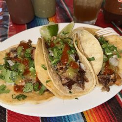 Carnitas tacos topped with fresh cilantro and diced onions, with salsa verde and spicy salsa roja. Ice-cold Tamarindo Jarritos on the side.