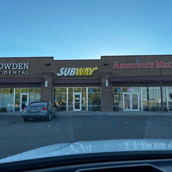 Subway - Front area - A shopping plaza with storefront signs for Subway, America’s Mattress, and Cowden Family Dental, with parked cars in front and a clear blue sky. - Fast Food Near Me - Rio Rancho, New Mexico