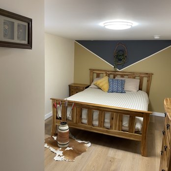 Stoked Homes - a bedroom with a bed, dressers, and a cow hide rug - General Contractors Near Me