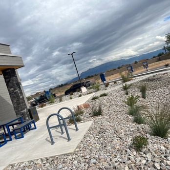 Dutch Bros Coffee - An outdoor scene featuring a parking lot with a few cars, a landscaped area with small plants and rocks, and mountains in the distance under cloudy skies. - Coffee & Tea Near Me - Albuquerque, New Mexico