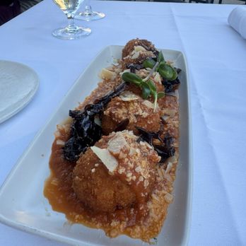 Cento - Arancini - A rectangular white plate holds fried arancini topped with sauce, cheese shavings, and microgreens, set on a white tablecloth at an outdoor restaurant. - Italian Near Me - Madison, Wisconsin