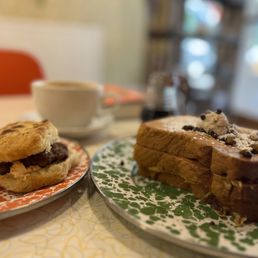 French Toast - A plate of cannoli French toast topped with chocolate chips and powdered sugar, alongside a sausage biscuit with chocolate filling, and a cup of coffee in the background.