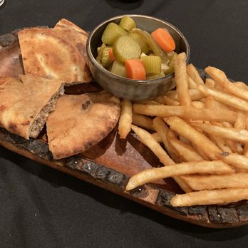 Cairo Kebab - Hawashi - A wooden serving platter contains a sliced meat-filled pastry, a portion of French fries, and a small bowl of pickled vegetables including cucumbers, carrots, and celery. The food is presented on a dark table, with the pastry cut into sections revealing the filling inside. The fries are golden and crispy, and the pickled vegetables add color to the dish. - Middle Eastern Near Me - Chicago, Illinois
