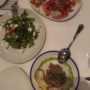 Prezza - Three dishes are displayed: a green salad with cheese, a plate of cured meats, and a meat dish with bread slices, on a white table. - Italian Near Me - Boston, Massachusetts