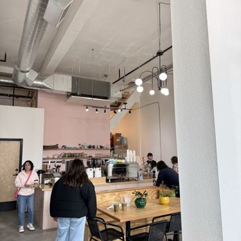 Kainos Coffee - A bright coffee shop features minimalist decor, a wooden counter, and several customers ordering or sitting. Potted plants are on the table. - Coffee Roasteries Near Me - Gresham, Oregon