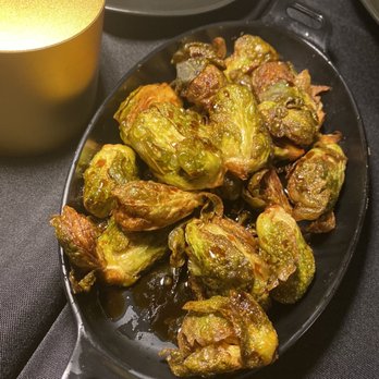 Flavorture - Roasted Balsamic Brussels - A black oval dish contains roasted Brussels sprouts with a caramelized appearance, placed on a dark table. - Bars Near Me - Washington, DC, District of Columbia