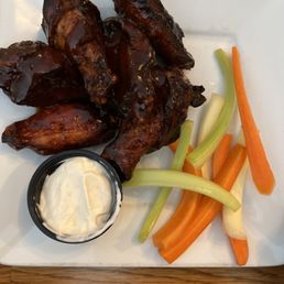 Maple bacon Bourbon wings - A plate of barbecue chicken wings served with celery and carrot sticks, accompanied by a side of creamy dipping sauce.