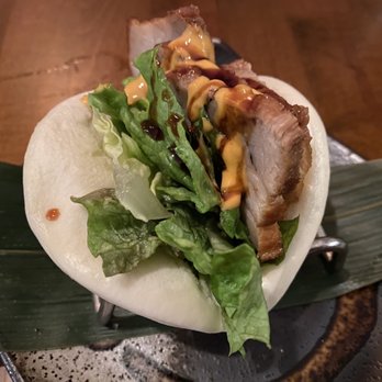 Wasan Brooklyn - "Chashu" Pork Bun - A steamed pork bun filled with lettuce, sliced pork, and drizzled with sauces, presented on a leaf and metal stand. - Japanese Near Me - Brooklyn, New York