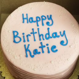 A round, gluten-free birthday cake with pale pink icing & white edible "pearls." The words "Happy Birthday Katie" are in the middle in blue. A round, gluten-free birthday cake with pale pink icing & white edible "pearls." The words "Happy Birthday Katie" are in the middle in blue.