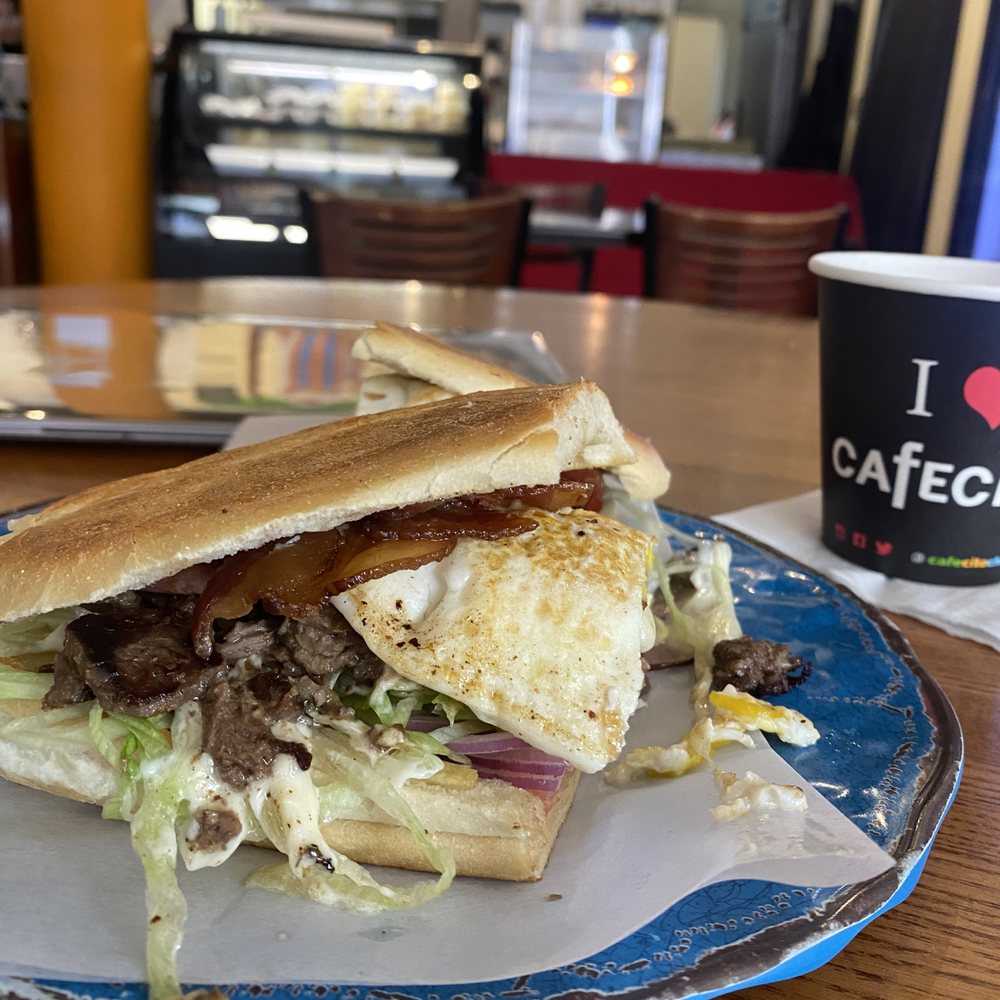 Cafecito - The Chivito Sandwich with everything on it. The single cafecito is in the background - Cuban Near Me - Chicago, Illinois Cafecito - The Chivito Sandwich with everything on it. The single cafecito is in the background - Cuban Near Me - Chicago, Illinois