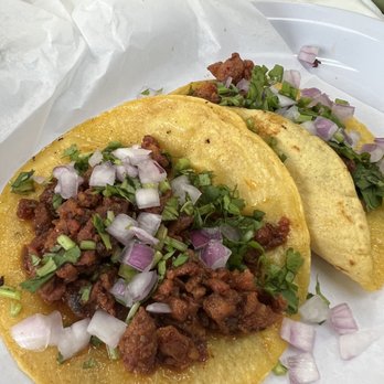 Best Taco - Adobada taco - Two tacos with corn tortillas are topped with seasoned meat, chopped onions, and cilantro. The tacos are served on white paper with some additional chopped onions and cilantro scattered around. The presentation suggests a casual dining setting, typical of Mexican eateries. - Mexican Near Me - Temple, Pennsylvania