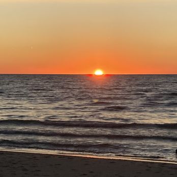 Rosemont Inn - A photograph captures a sunset over the ocean, with the sun positioned just above the horizon. The sky displays a gradient of colors from orange near the horizon to lighter shades higher up. Gentle waves ripple across the water, reflecting the sunset's colors. The sandy beach in the foreground is visible, with a small silhouette of an object or person on the right side. The scene emphasizes the natural beauty of the sunset and coastal environment. - Bed & Breakfast Near Me - Douglas, Michigan