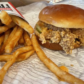 KFC - Spicy Chicken Sandwich Combo - A fried chicken sandwich with pickles and sauce on a bun, served with a side of French fries in a paper container. - Chicken Wings Near Me - Springfield, Oregon
