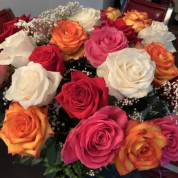 2 dozen roses for mom - A bouquet of roses in various colors including pink, white, red, and orange, accented with small white baby's breath flowers, arranged on a table in an indoor environment with chairs and a cabinet in the background.