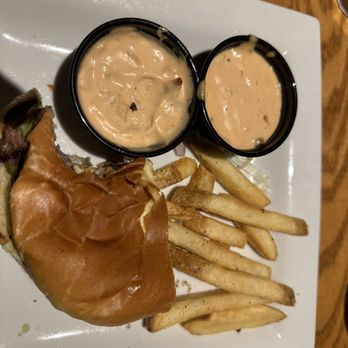 Chili's - Half order of a smash burger and fries. - A meal includes a burger with a bun, French fries, and two small cups of creamy dipping sauce on a white square plate. The plate is placed on a wooden table, and the image is taken from an overhead angle. - Bars Near Me - Lone Tree, Colorado