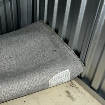 Go Store It Self Storage - A fabric cushion with dirt and stains is positioned in a storage unit corner, leaning against a metal wall and a wooden floor. - Self Storage Near Me - Cincinnati, Ohio