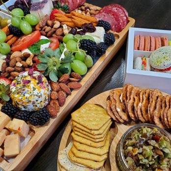 Macaron Delights - Quarantine bubble party - A cheese and charcuterie platter with grapes, nuts, sliced tomatoes, and cheese, accompanied by a box of macarons and cookies, displayed on a dark table. - Macarons Near Me - Lorton, Virginia