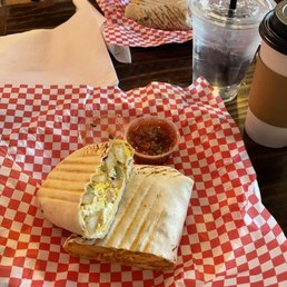 Breakfast Burrito - A breakfast burrito cut in half with salsa, a paper cup of coffee, and a water cup on a checkered paper at a cafe table.