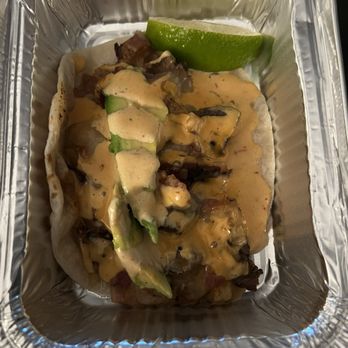 Taco Madre - Mayan Taco - so freaking good - A taco filled with meat, avocado slices, and sauce, served in a foil container with a lime wedge on the side. - Tacos Near Me - Montgomery, Illinois
