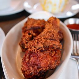 Southern Fried Chicken Plate - Two pieces of fried chicken are placed on a white dish, with a bowl of sauce nearby. The background shows a cupcake and other tableware.