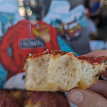 Izzy's Pizza Bus - a hand holding a piece of pizza - Food Trucks Near Me - Omaha, Nebraska