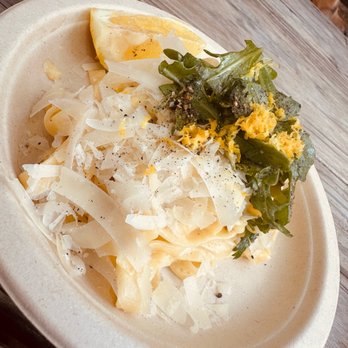 Patrizi's - Lemon and thyme pasta - A disposable plate holds pasta topped with cheese, a lemon wedge, and a side of greens with shredded egg, on a wooden table. - Italian Near Me - Austin, Texas