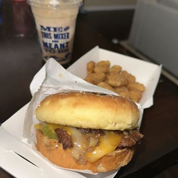 Culver's - Meal - A cheeseburger with melted cheese, pickles, and onions in a bun, accompanied by a side of fried chicken nuggets and a vanilla milkshake with a blue straw. - Burgers Near Me - Brandon, Florida