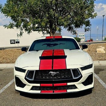 The Wrap Lab - A white Ford Mustang with red racing stripes is parked in a parking lot beneath a large tree, with a building and sky in the background. - Vehicle Wraps Near Me - Albuquerque, New Mexico