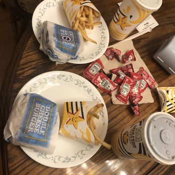 Hardee's - Double Cheeseburger Combo - The image shows two fast food meals on a wooden table, each with a burger wrapped in branded paper labeled 'Double Cheeseburger.' One burger has a side of French fries in a branded container, and there are multiple ketchup packets scattered on the table. Two large soft drinks in branded cups with straws are also present, along with a paper napkin. The setting appears to be a casual dining or takeout environment. - Fast Food Near Me - Indianapolis, Indiana