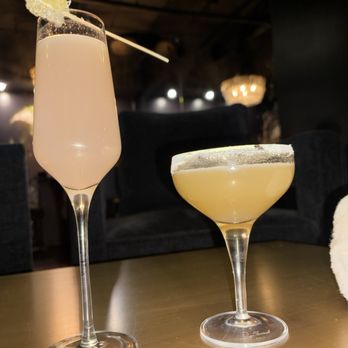 Dearly Beloved - Drinks! - Two cocktails in elegant glasses are placed on a table in a dark, ambient setting, likely a bar or cocktail restaurant. - Cocktail Bars Near Me - Chicago, Illinois