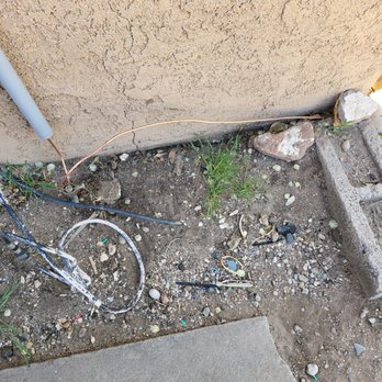Copper Sun Electric - Wires and debris are visible on the dirt ground next to a building wall, with some rocks and small plants present. - Electricians Near Me