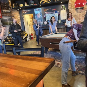 Fulton Hall - a group of people playing pool - A group of people are playing pool in a sports bar decorated with sports memorabilia, brick walls, and a bar counter. - Pubs Near Me - Brooklyn, New York