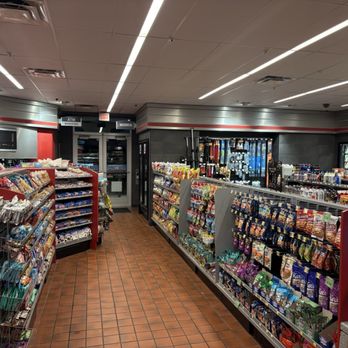 QuikTrip - The image shows the interior of a convenience store with aisles stocked with snacks, chips, and other packaged foods. Beverage refrigerators are visible in the background, along with vending machines and an ATM. The store has a tiled floor, a drop ceiling with linear lighting, and signs indicating the location of restrooms and an ATM. The overall setting suggests a typical convenience store layout designed for quick shopping and refreshment options. - Gas Stations Near Me - Lindale, Texas