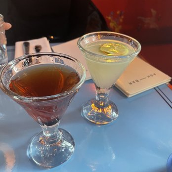 Ash Bar - Manhattan and rhum daquiri - Two cocktails in martini glasses, one dark and one light with lemon garnish, are on a table at a restaurant or bar setting. - Cocktail Bars Near Me - Baltimore, Maryland