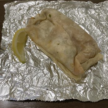 La Costa - A burrito wrapped in a soft flour tortilla is resting on crinkled aluminum foil, with a lemon wedge placed nearby. The setting suggests it is from a Mexican restaurant or takeout service, with the foil used for serving or packaging. The background shows a dark surface, possibly a table or counter. - Mexican Near Me - Tracy, California
