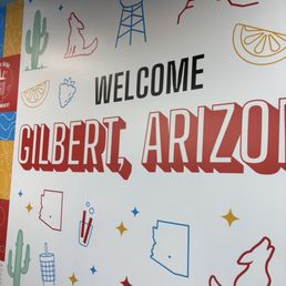 A large welcome sign for Gilbert, Arizona, features colorful illustrations of cacti, mountains, and desert elements.