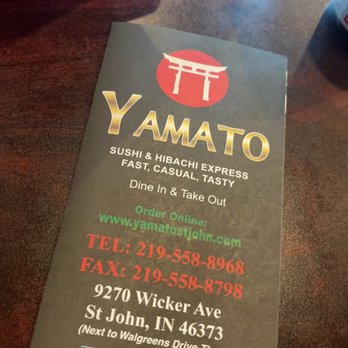 Yamato - A printed menu from Yamato, a sushi and hibachi restaurant in Saint John, Indiana, is shown on a dark wooden table. The menu displays the restaurant's name, logo, and description of offerings, including dine-in and takeout options. It provides the address, phone numbers, fax number, and website, along with hours of operation and a Facebook link. A water bottle and part of a beverage container are visible on the table. - Sushi Bars Near Me - Saint John, Indiana
