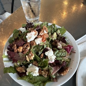 Holy Burgers - Half beet salad - A mixed green salad with cheese crumbles and nuts is served on a white plate, accompanied by a glass of water with ice and a straw. - Burgers Near Me - Albuquerque, New Mexico