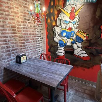 Devil Dawgs - I call this the Gundam VIP area - A corner of a restaurant features a mural of a Gundam robot holding a hot dog, with red chairs and a rustic brick wall. - Hot Dogs Near Me - Chicago, Illinois