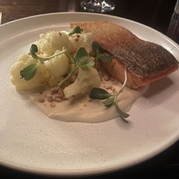 Trout - A dish with a piece of cooked fish with crispy skin, served with cauliflower florets, microgreens, and a creamy sauce on a white plate.